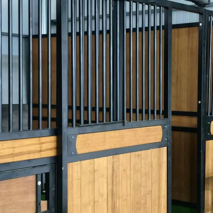 A horse stall constructed with a combination of metal framework and wooden panels, featuring a decorative curved top and a small access door.