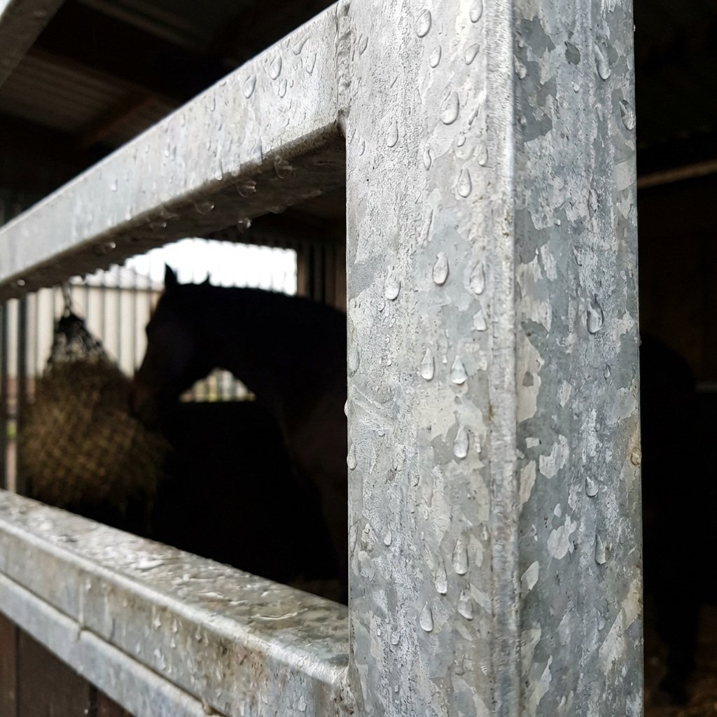 hyperrealistic product photography macro shot of hot-dip galvanized steel framework of a horse stall, zinc coating texture visible, rain water beading on the surface, structural steel beams, horse silhouette in the background inside the stable, emphasizing durability against rust and UV, 16:9 aspect ratio, no text, no letters, no typography --ar 16:9 --style raw --v 6.0